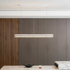 A Clérachic linear chandelier of clear glass segments glowing above a marble dining counter, with a dark bowl and a tumbler below.