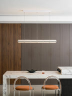 Compact Clérachic glass chandelier lit above a marble breakfast bar with two clear-backed stools and orange cushions.