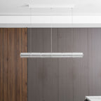 Unlit chrome and clear glass chandelier from Clérachic hung against a grey-brown panelled wall, with a ribbed walnut panel on the left.