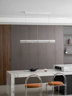 Switched-off Clérachic glass chandelier above a marble counter, with a dark bowl and a shelf of bottles in the background.