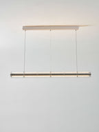 Lit Clérachic glass chandelier hanging from a white ceiling canopy on three cables, with warm light grazing the ceiling above.