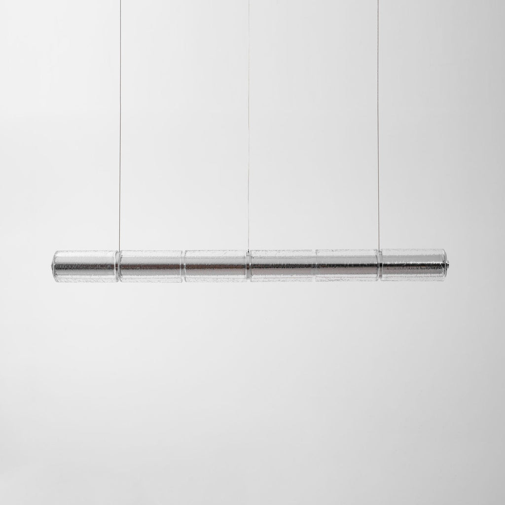 Clear segmented glass chandelier from Clérachic hung on thin cables against a soft grey backdrop, shown unlit.