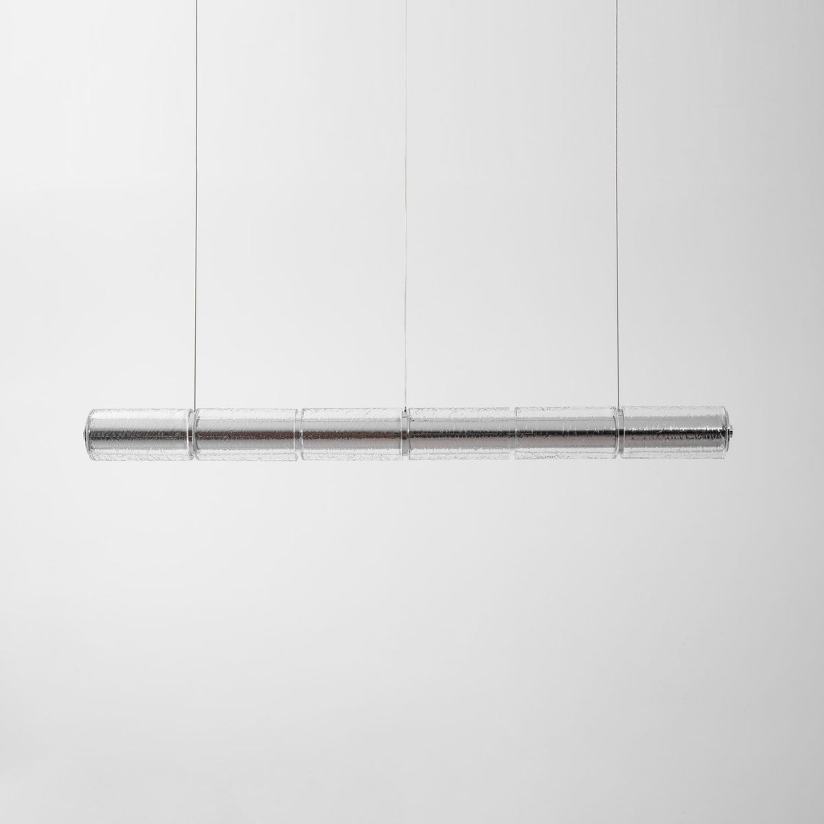 Clear segmented glass chandelier from Clérachic hung on thin cables against a soft grey backdrop, shown unlit.