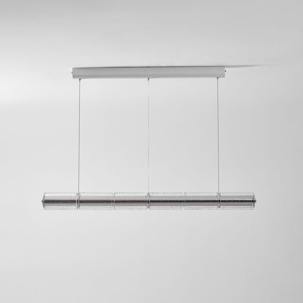 This Clérachic glass chandelier hangs from a chrome ceiling bar on three cables, shown unlit against a pale grey wall.