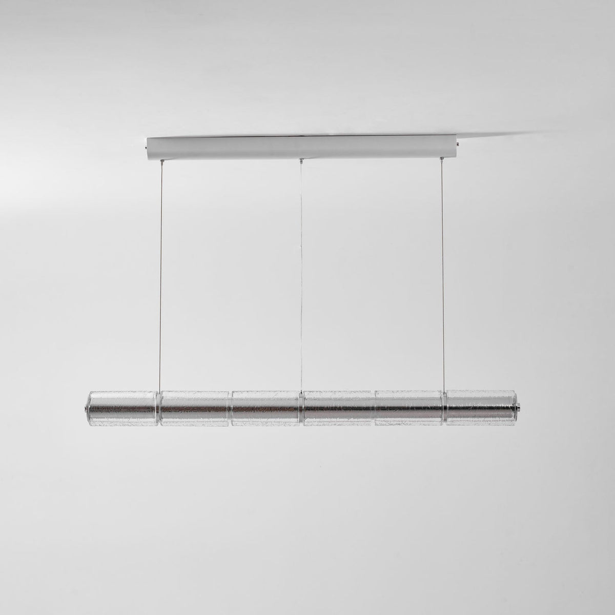 This Clérachic glass chandelier hangs from a chrome ceiling bar on three cables, shown unlit against a pale grey wall.