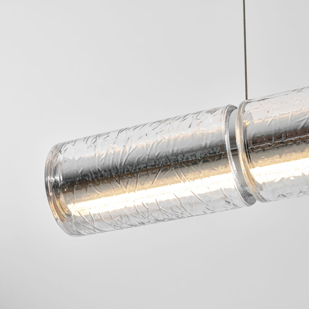 Close view of a lit glass segment of this Clérachic chandelier, the crackled clear glass glowing warm inside with a chrome collar.