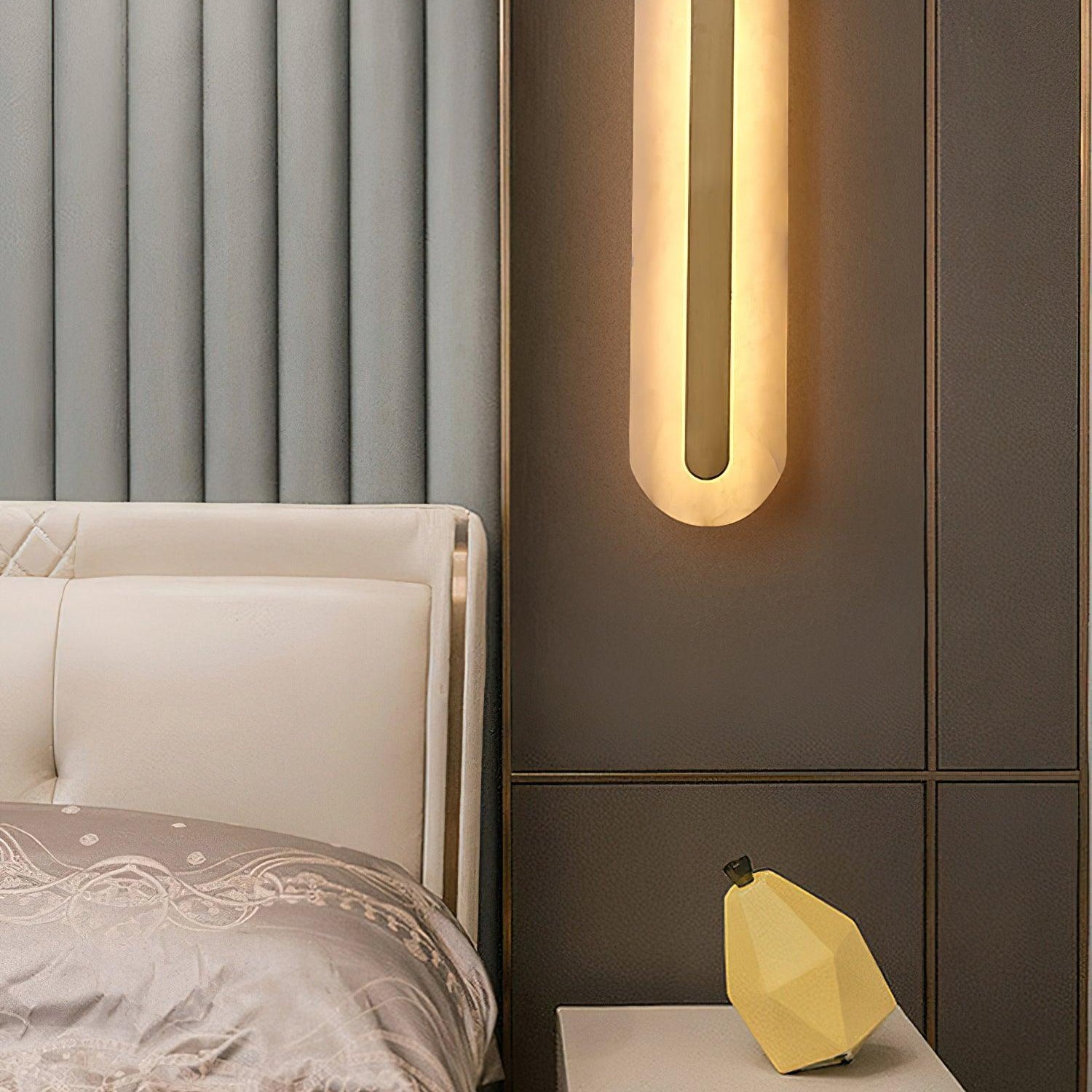 The Clérachic Selvia sconce lit above a bed on a panelled taupe wall.