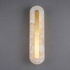 Clérachic Selvia wall light lit on grey, brass strip glowing down the alabaster face.