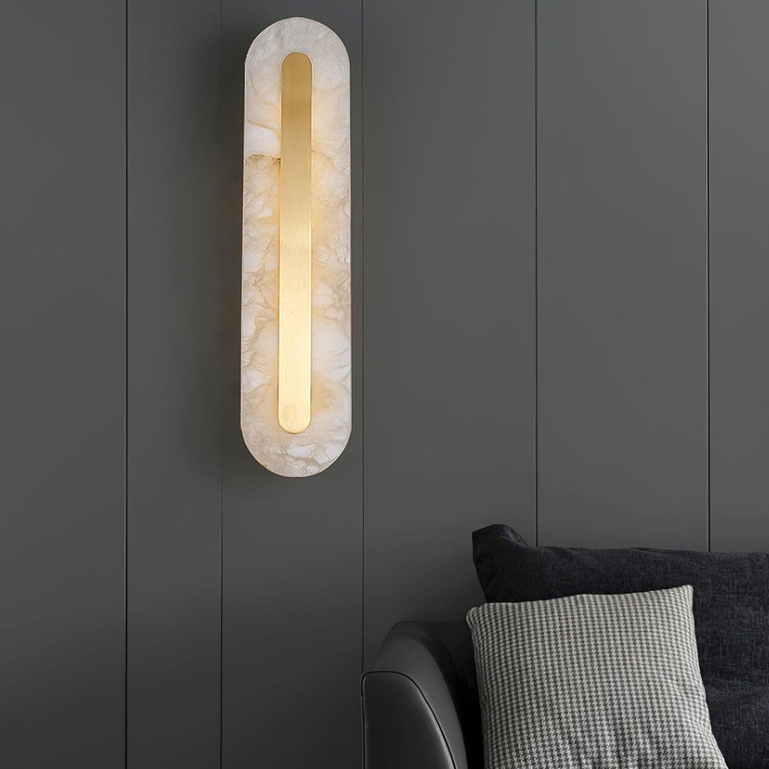 Clérachic Selvia sconce lit on charcoal panelling above a dark grey sofa.