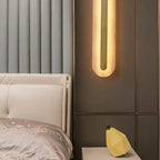 The Clérachic Selvia wall light glowing on a bronze panel beside an upholstered bed.