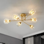 Clérachic sputnik chandelier in all-gold, six transparent globes lit over a modern room with dark slatted screens behind.