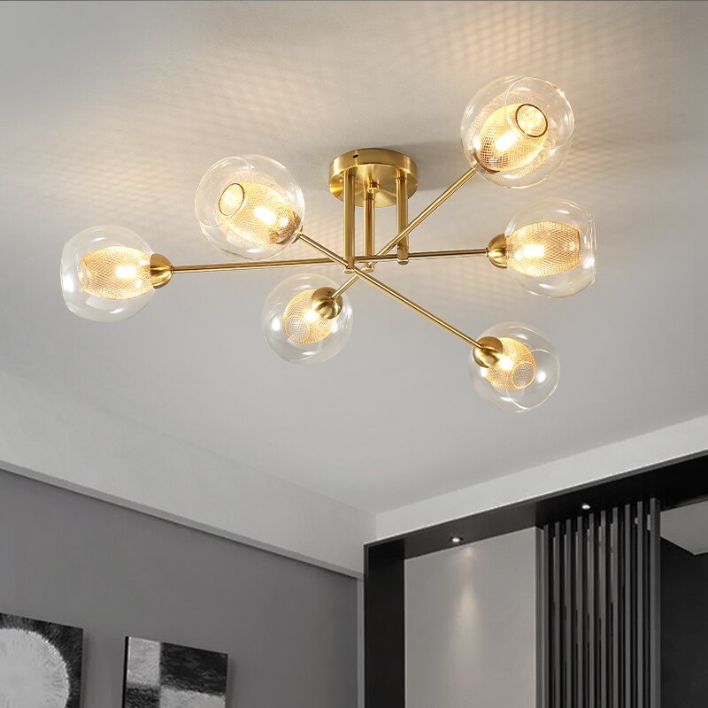 Six transparent globes on the gold Clérachic sputnik chandelier, lighting a corner where framed prints hang below.