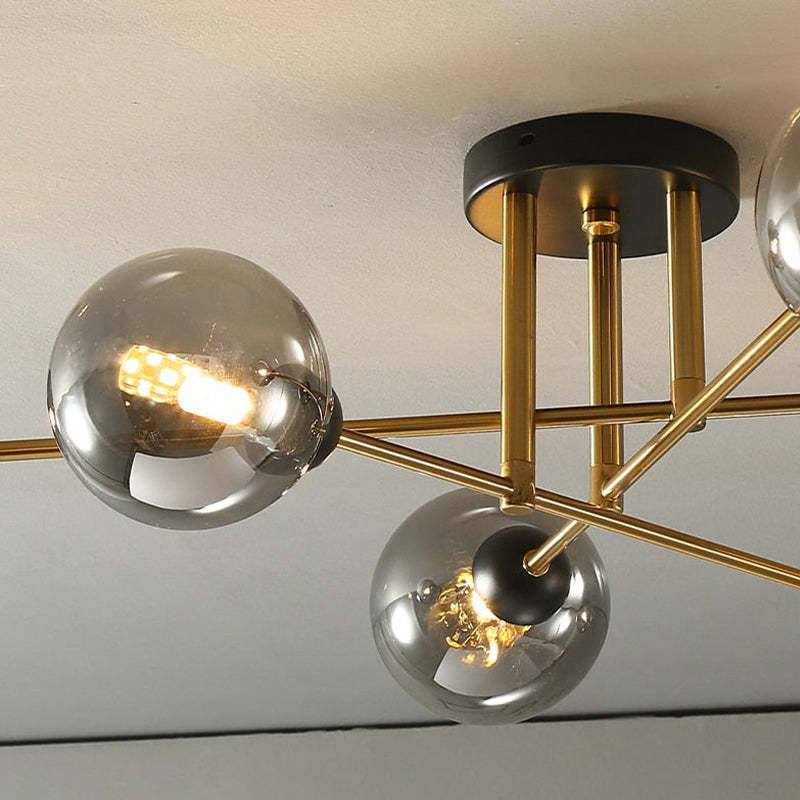 Detail of the black canopy and short gold stems on the Clérachic sputnik chandelier, a lit G9 lamp visible inside a grey globe.