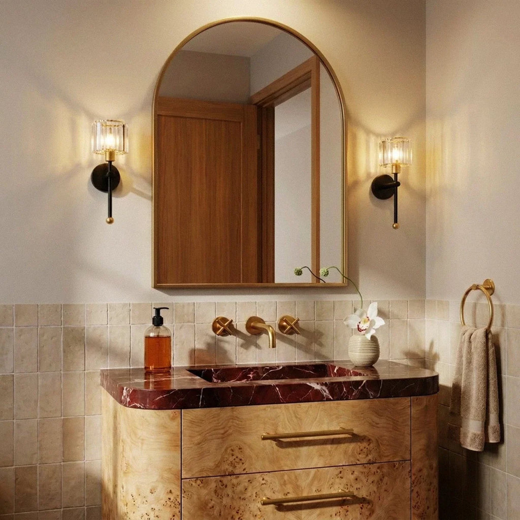 Clérachic pair of black and brass wall lamps with ribbed glass shades either side of an arched brass mirror above a marble basin.