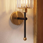 Clérachic close view of a black stem, brushed brass backplate and ball finial under a clear ribbed glass shade on plaster.