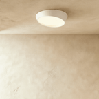 Clérachic low-profile round ceiling light in white with a tilted frosted diffuser lit warm, mounted on a limewash ceiling.