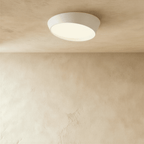 Clérachic slim white ceiling light with a lit frosted diffuser in a slanted rim, photographed from below on a limewash ceiling.