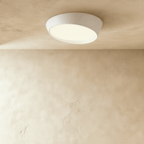 Clérachic larger white round ceiling light with an angled iron body and a softly lit frosted diffuser on a limewash ceiling.