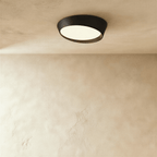 Clérachic round ceiling light with a matte black iron rim and a warm-lit frosted diffuser on a limewash ceiling.