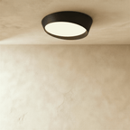 Clérachic wide black round ceiling light with a tilted frosted acrylic diffuser and a deep matte iron rim on a limewash ceiling.