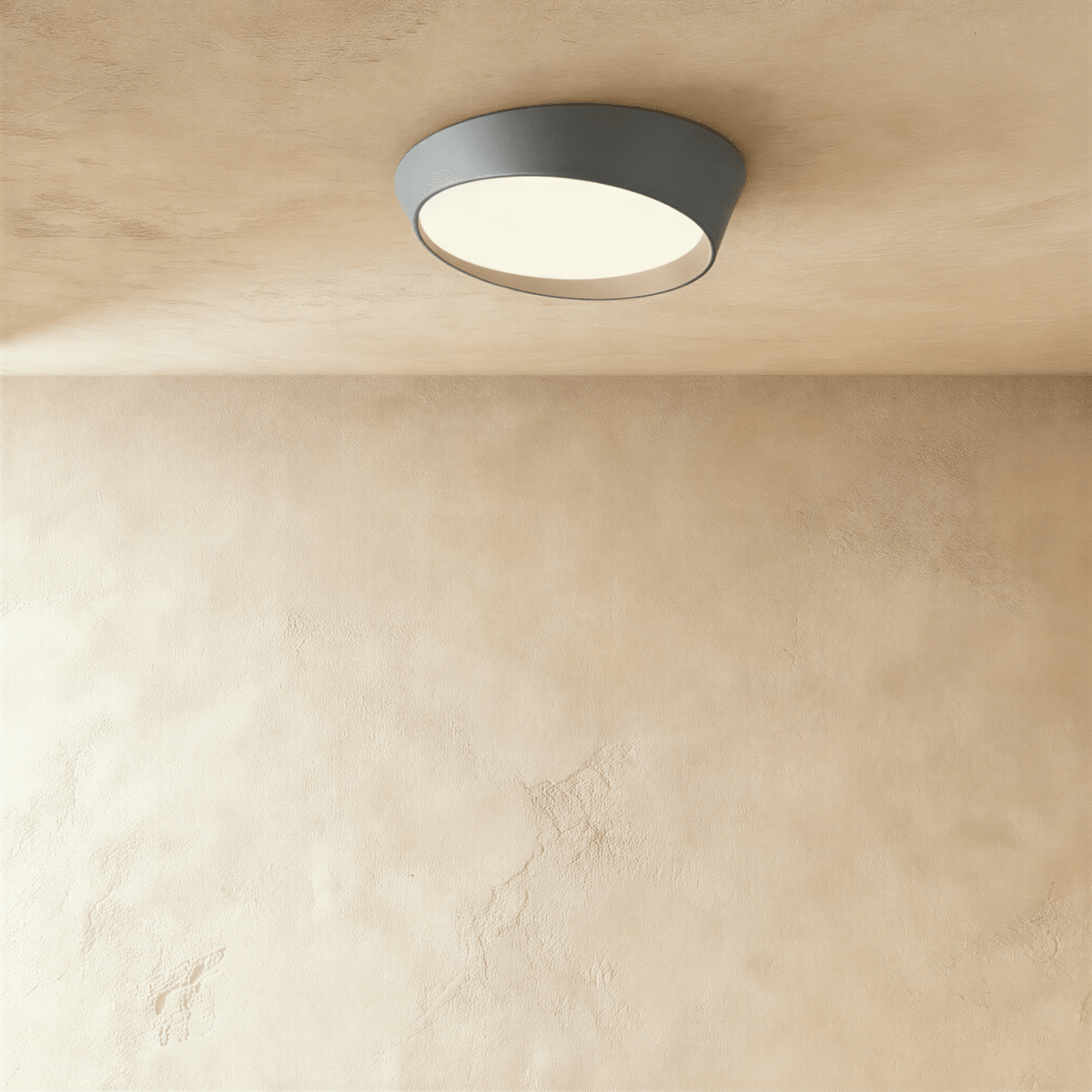 Clérachic round ceiling light in mid grey with a slanted rim and a warm-lit frosted diffuser, mounted on a limewash ceiling.