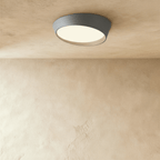 Clérachic grey low-profile ceiling light with an angled iron rim and a softly glowing frosted diffuser on a limewash ceiling.