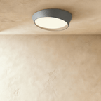 Clérachic large grey round ceiling light with a pale inner rim and a frosted diffuser lit warm, seen from below on limewash.