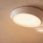 Close view of the Clérachic white ceiling light, its angled rim and frosted diffuser glowing warm on a softly textured ceiling.