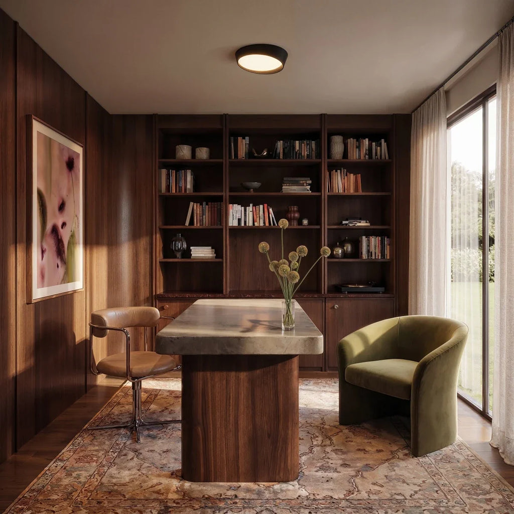 Clérachic black round ceiling light with a warm-lit diffuser over a study with walnut shelving, a desk and an olive armchair.