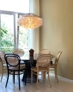 Clérachic shell chandelier in a dining corner with bentwood cane chairs, a round table and a mustard-yellow wall.