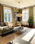 Clérachic shell chandelier in a sunlit living room with olive-green walls, a grey sofa and a low dark coffee table.