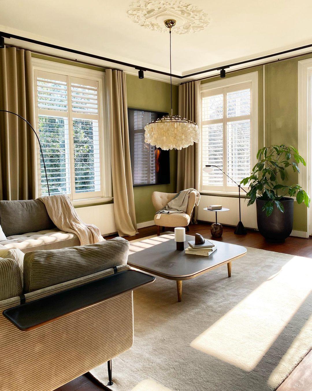 Clérachic shell chandelier in a sunlit living room with olive-green walls, a grey sofa and a low dark coffee table.