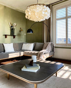 Clérachic shell chandelier above a dark coffee table and grey corner sofa, with an arched black floor lamp beside it.