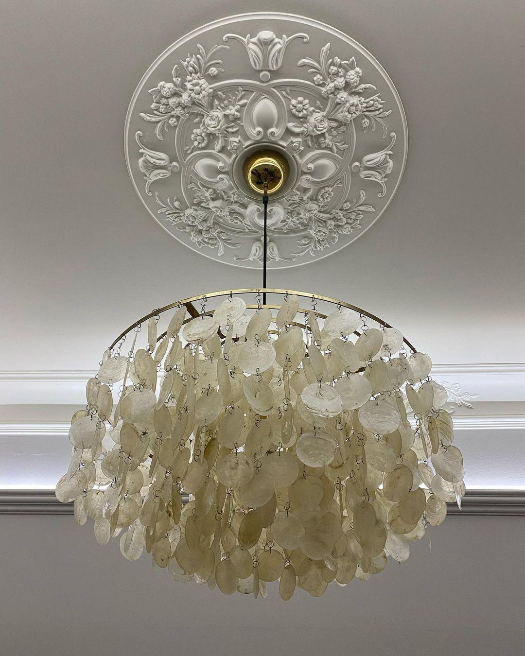 Looking up at a Clérachic shell chandelier hung from a carved white ceiling rose, its discs in warm cream.