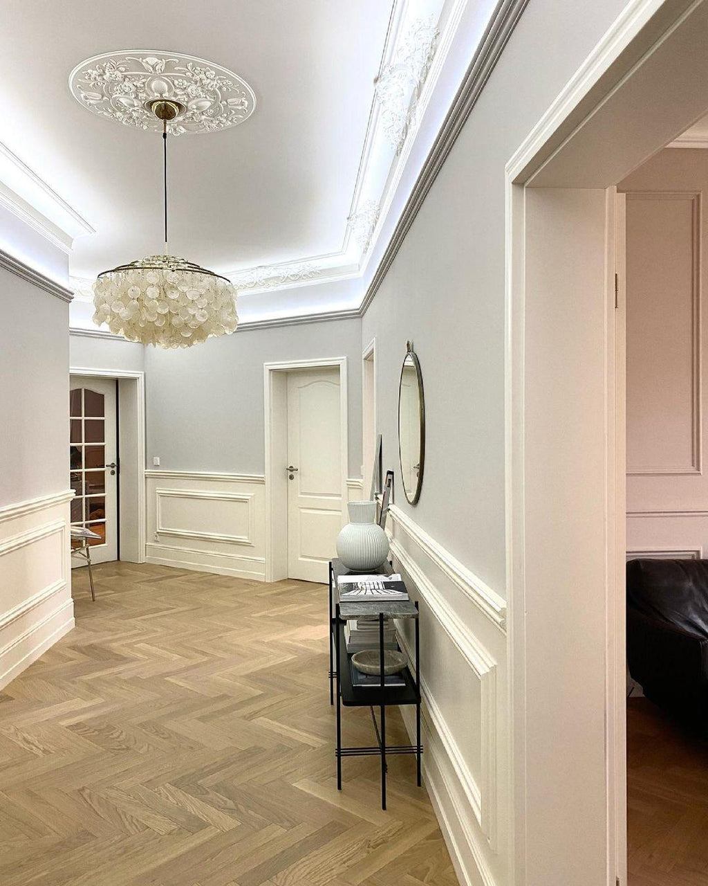 Clérachic shell chandelier seen down a long hallway with a herringbone oak floor and a carved ceiling rose overhead.