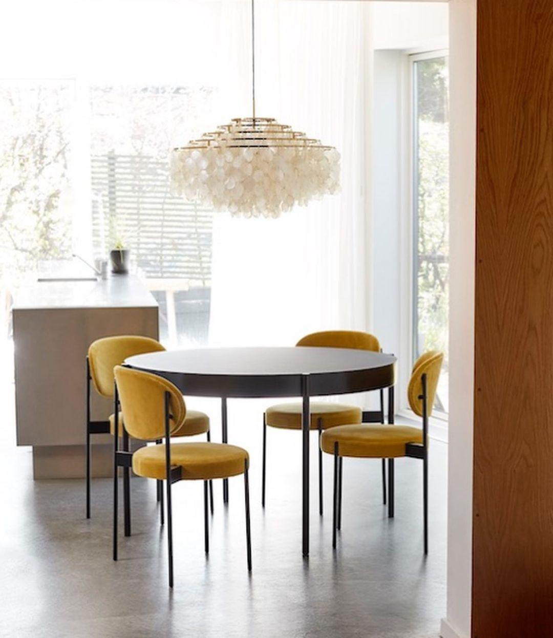 Gold-ringed Clérachic shell chandelier above a round black table and mustard velvet chairs, by a large window.