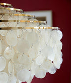 Close view of the gold rings and hanging shell discs of this Clérachic chandelier against a deep red wall.