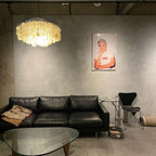 Lit Clérachic shell chandelier in a concrete-walled room with a black leather sofa and a glass coffee table.