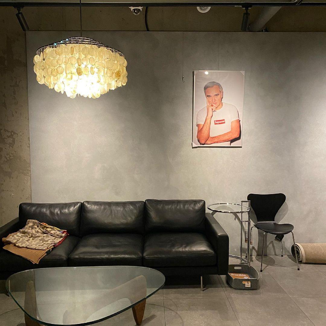 Lit Clérachic shell chandelier in a concrete-walled room with a black leather sofa and a glass coffee table.