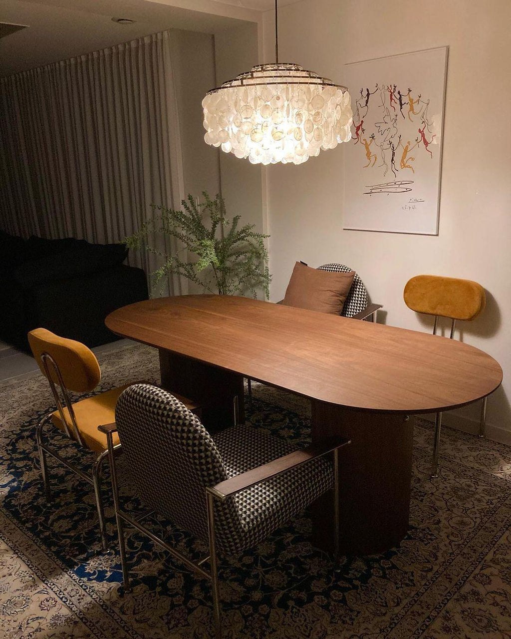 Clérachic shell chandelier glowing above an oval walnut table, with mustard chairs and a patterned rug beneath.
