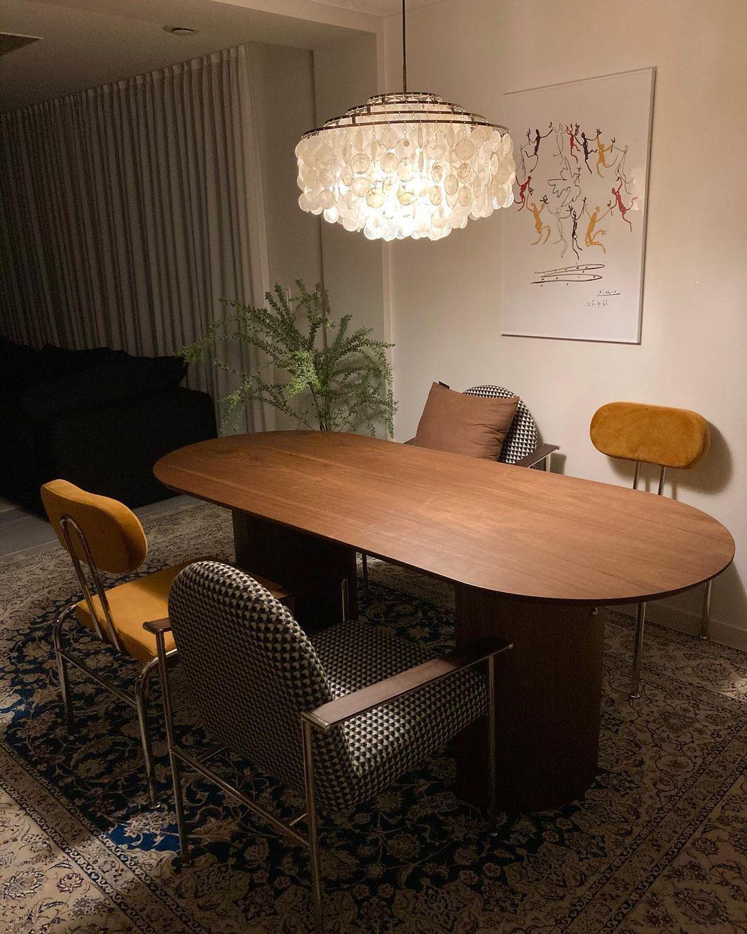 Clérachic shell chandelier glowing above an oval walnut table, with mustard chairs and a patterned rug beneath.