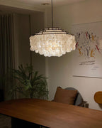 Closer view of a lit Clérachic shell chandelier over a walnut table, with a fern and a line-drawing print behind.