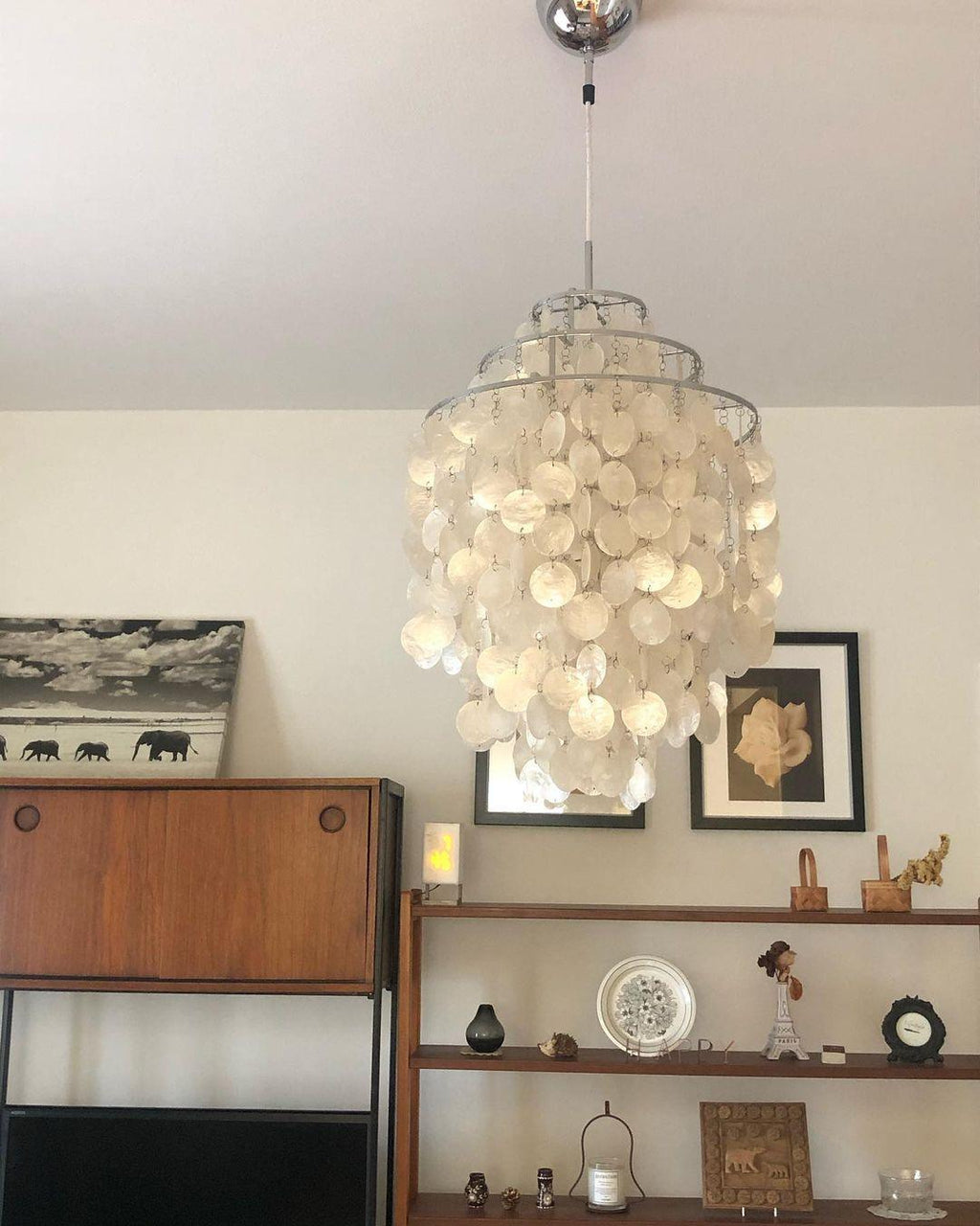 Chrome-capped Clérachic shell chandelier in a long spiral of white discs, hung beside a teak sideboard and shelves.