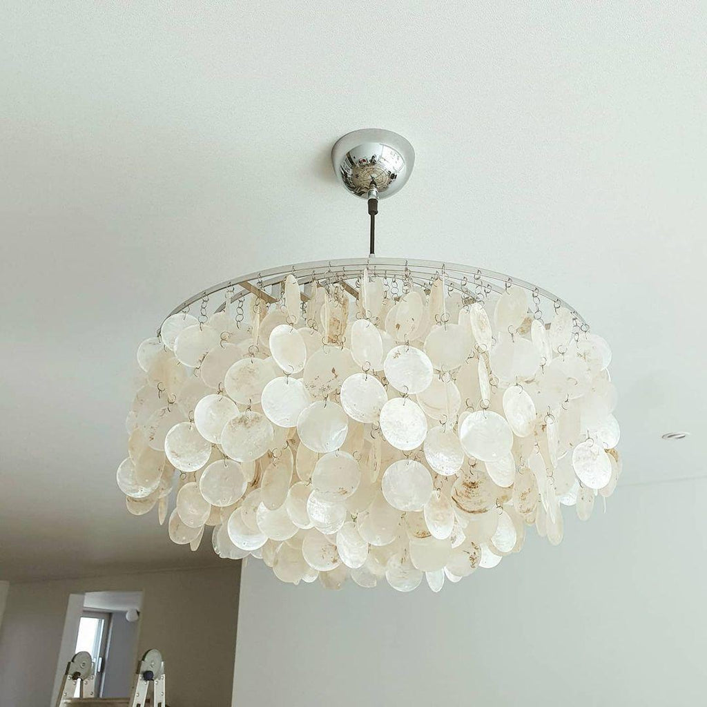 Looking up at a Clérachic shell chandelier with a chrome ceiling cap, its overlapping white discs filling the frame.