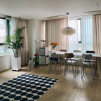 Small Clérachic shell chandelier far across a bright dining room with a blue hexagon rug, a tall palm and white table.
