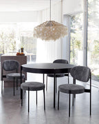 Gold-ringed Clérachic shell chandelier above a round black table and grey upholstered chairs, with glass doors beyond.