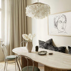 Clérachic shell chandelier over an oval pale table and bentwood chairs, beside a line-drawing portrait and linen curtains.