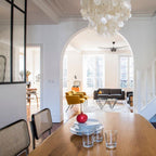 Clérachic shell chandelier at the edge of the frame, seen through an arch beyond a wooden table set with plates and glasses.
