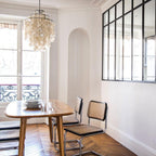 Clérachic shell chandelier in a Parisian dining room with a herringbone floor, a black-framed glass partition and cane chairs.