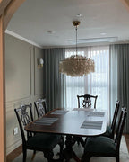 Clérachic shell chandelier above a dark wood dining table with carved chairs in a grey-green panelled room.